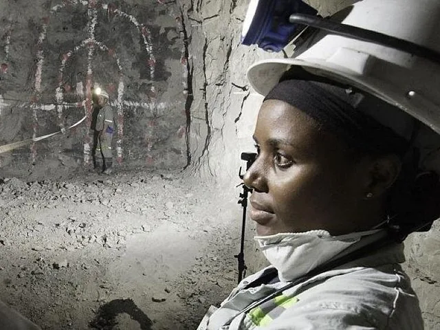 A miner in a hard hat inside an underground tunnel with marked rock walls.