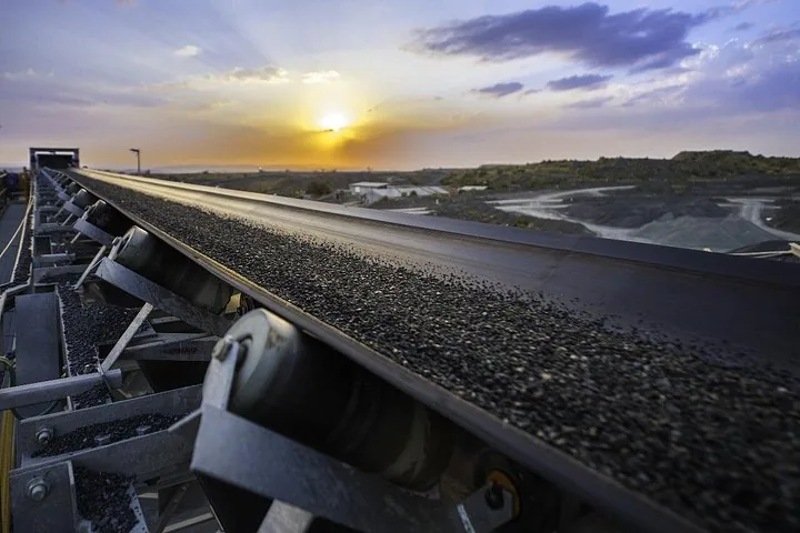 Una cinta transportadora que lleva roca triturada en una mina al atardecer.