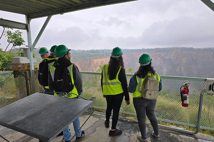 Un groupe de personnes portant des casques verts observant une grande mine à ciel ouvert.